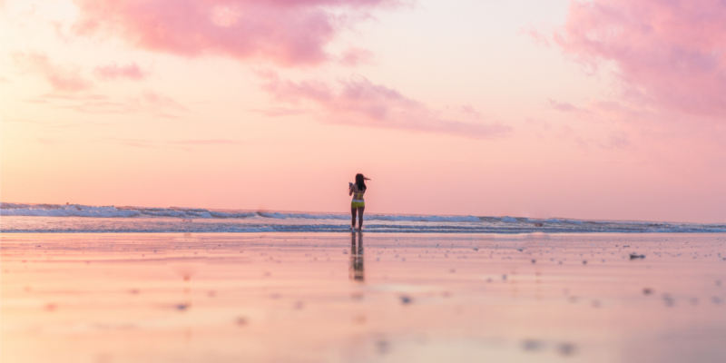Woman standing in the surf at sunrise as part of her self-care ritual.
