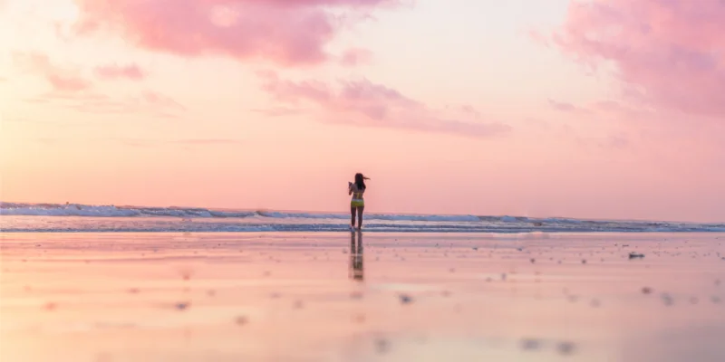 Woman standing in the surf at sunrise as part of her self-care ritual.