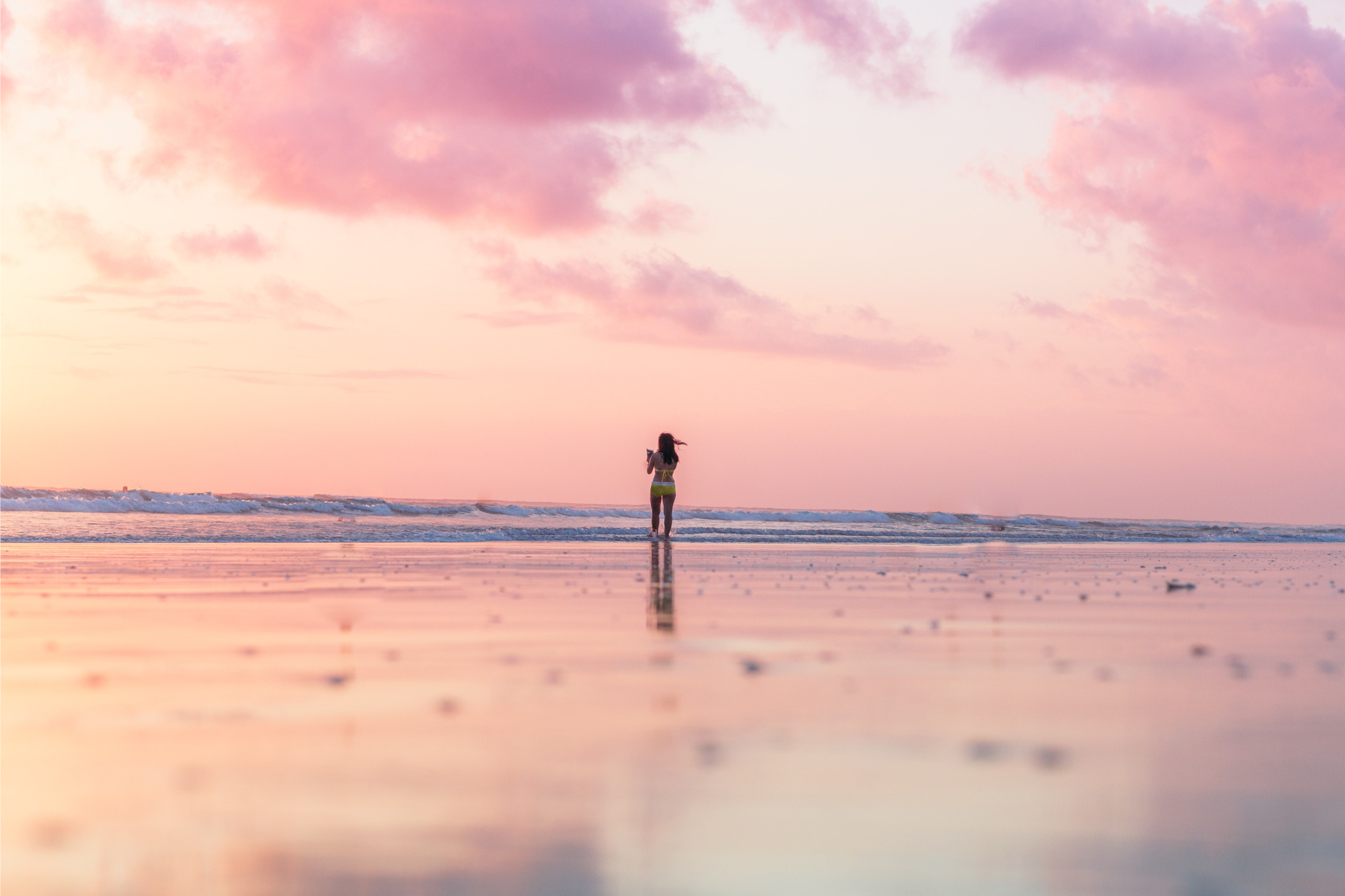 Woman standing in the surf at sunrise as part of her self-care ritual.