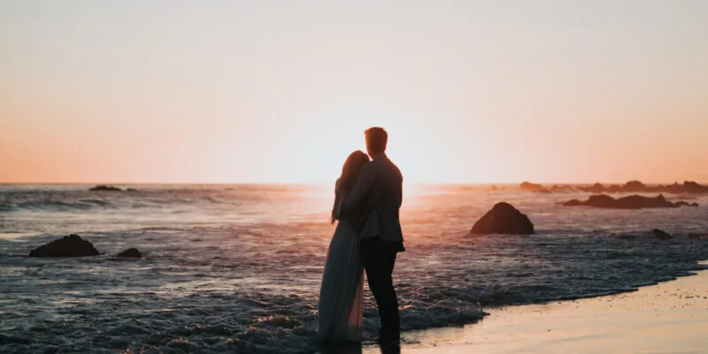 Couple standing in the surf and embracing as the watch the sunset.
